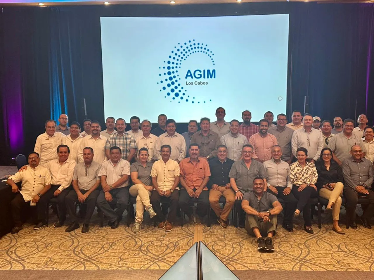 Socios de AGIM Los Cabos reunidos frente a la pantalla con el logotipo de la asociación