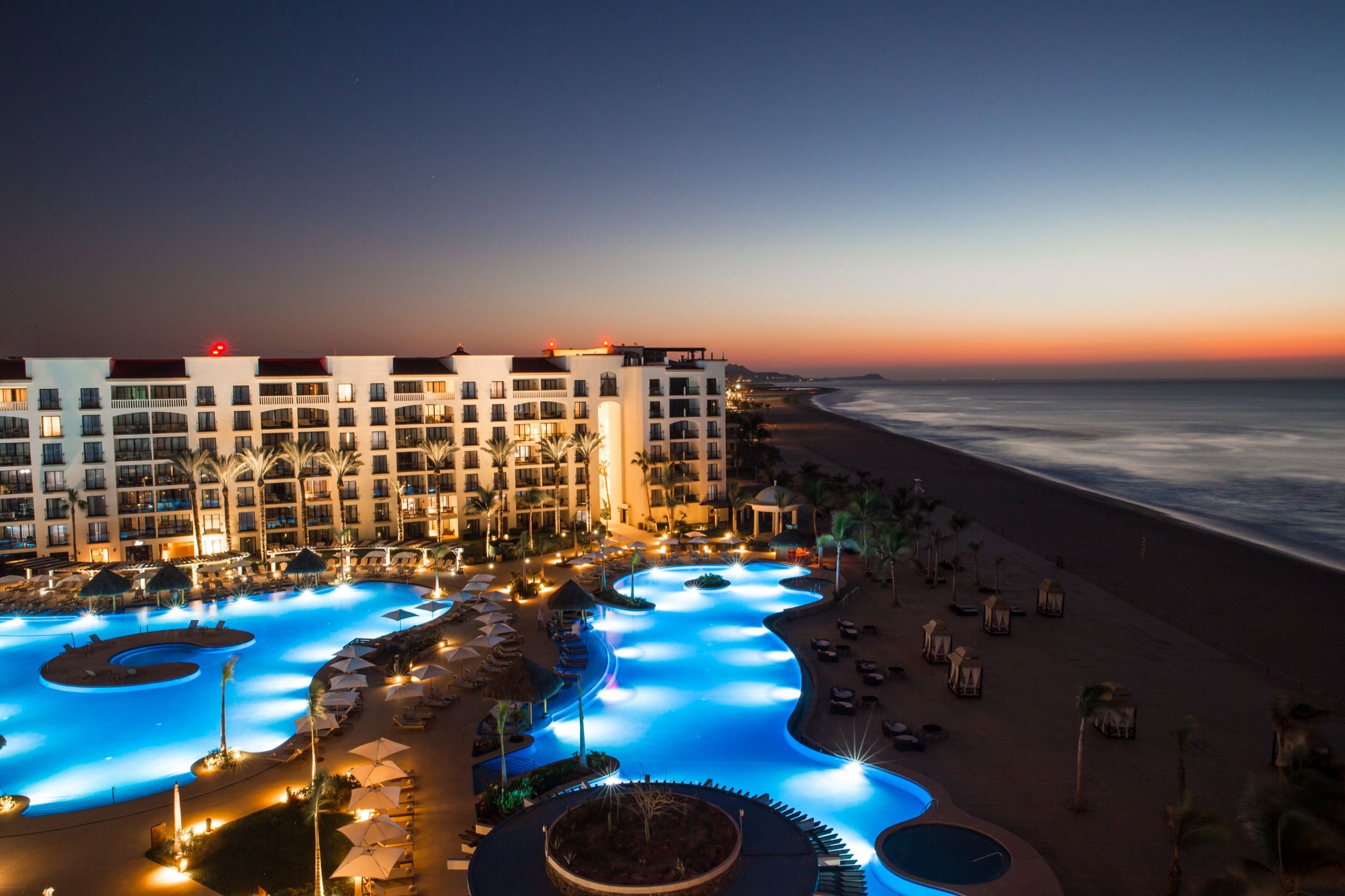Vista nocturna de las albercas iluminadas y la playa del hotel Hyatt Ziva Los Cabos